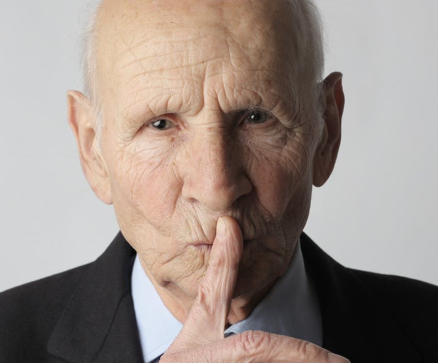 elderly gentleman making silence gesture in studio